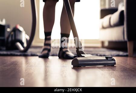 Aspirateur. Homme nettoyant le sol à la maison et faisant des tâches ménagères dans un appartement moderne. Lumière du soleil de la fenêtre. Bonne personne passant l'aspirateur dans le salon. Banque D'Images