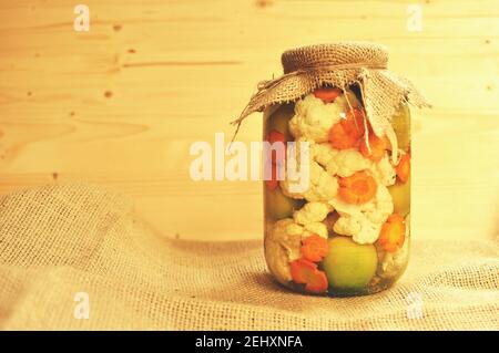 Concept d'un pot de cornichons de saison avec tomates vertes de couleur, carottes d'orange et chou-fleur blanc sur fond de bois naturel. Copier le texte. Banque D'Images