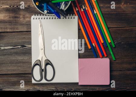 des ciseaux sont couillés sur un carnet ouvert et des crayons de couleur vue sur une table en bois Banque D'Images