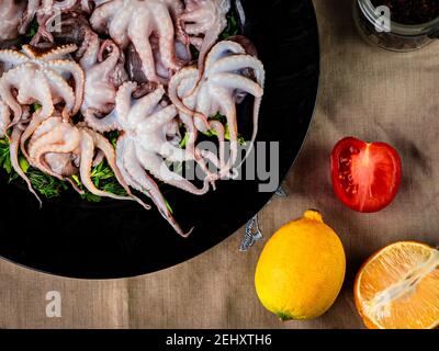 Poulpe de bébé crue dans une assiette noire. Fruits de mer biologiques. Vue de dessus. Banque D'Images