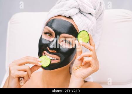 Femme avec un masque facial au charbon de bois noir et des tranches de concombre. Soins de beauté Banque D'Images