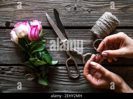 Des mains de femmes faisant le bouquet sur une table en bois avec des fleurs de rose Banque D'Images