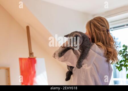 Femme peintre d'art tenant son chat mignon en studio. Femme artiste essayant de trouver l'inspiration avant de peindre. Britannique shorthair chat et propriétaire d'animal de compagnie Banque D'Images