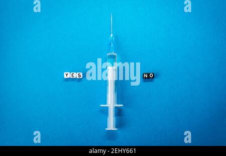 Oui non mots faits de lettres carrées et d'une seringue sur fond bleu. Avantages et inconvénients du vaccin contre le coronavirus, inquiétudes et doutes quant à la vaccination Banque D'Images