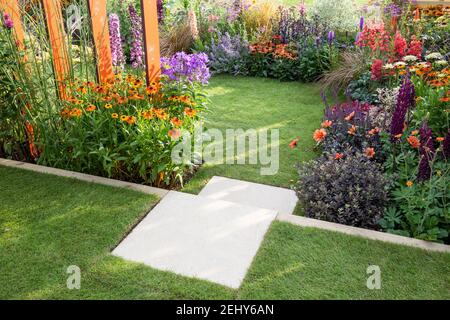 Un petit jardin - marches en pierre menant à un pelouse herbe avec parterres remplies de fleurs plantes y compris Helenium - Dahlias Angleterre GB Royaume-Uni Banque D'Images