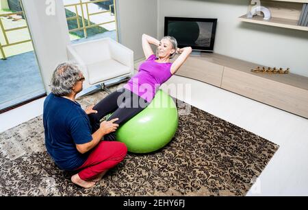 Entraînement actif de couple de personnes âgées avec Swiss ball à la maison - Les retraités font de l'exercice physique dans le salon de la salle de gym - homme mature entraîneur dame Banque D'Images