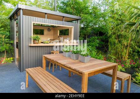 Jardin urbain extérieur espace de vie cuisine bar maison d'été sur le patio pavé de pierre en graphite foncé, banc de jardin mobilier de table, menthe en pots UK Banque D'Images