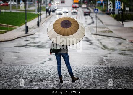 Femme avec un parapluie debout dans la rue de la ville sous la pluie. Voitures défocacées sur route à distance. Vue arrière d'une femme portant un Jean, une veste en cuir avec sac o Banque D'Images