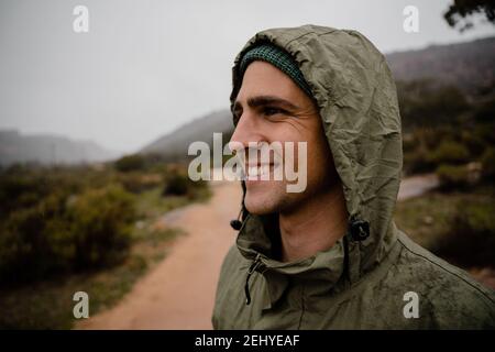 Souriant beau jeune athlète masculin heureux avec vue sur la montagne veste de pluie path pour une projection par temps froid Banque D'Images