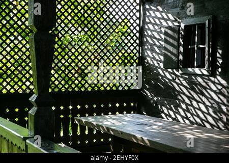 Un intérieur en bois éclairé par le soleil du porche d'une maison avec des branches et des feuilles à l'extérieur. Banque D'Images