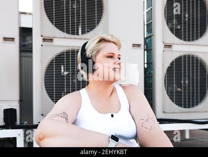 Femme souriante aux courbes et aux vêtements de sport assise sur le toit Banque D'Images