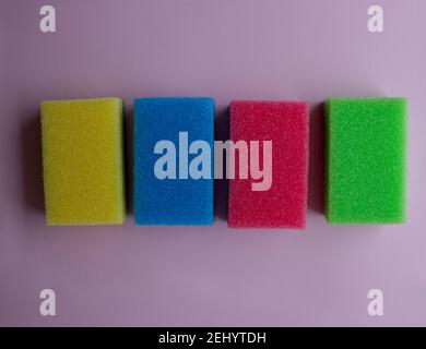 Quatre éponges en caoutchouc mousse colorées pour le nettoyage et le lavage de la vaisselle sur fond rose. Banque D'Images