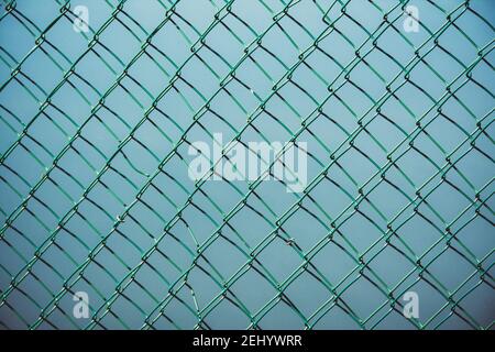 Clôture à maillons de chaîne sur un fond bleu créant un motif géométrique dans un environnement urbain Banque D'Images