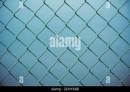Clôture à maillons de chaîne sur un fond bleu créant un motif géométrique dans un environnement urbain Banque D'Images