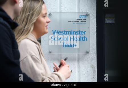 Londres, Angleterre, Royaume-Uni. 20 février 2021. Un homme et une femme se promènent devant le soupir « Westminster School Health Team », devant le bâtiment Westminster School Healthcares Service de Soho. Le Premier ministre Boris Johnson devrait annoncer lundi la date d'ouverture des écoles en Angleterre comme première étape de la feuille de route pour sortir du confinement actuel du coronavirus. Credit: Tayfun Salci/ZUMA Wire/Alay Live News Banque D'Images