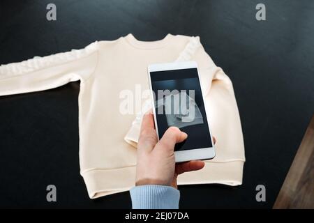 Vendre en ligne sur Internet. Boutique en ligne. Femme prenant des photos de vêtements sur un smartphone. Vendre des produits en ligne sur des Marketplaces Banque D'Images