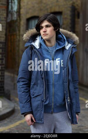 Jeune homme en vêtements de sport décontractés et manteau d'hiver. Portrait sur toute la longueur du corps avec un arrière-plan urbain. Banque D'Images