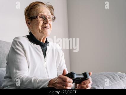 Crop anonyme 90 ans femme assis sur le canapé avec contrôleur moderne et jeux vidéo à la maison Banque D'Images