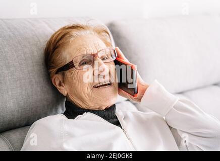 Une femme de 90 ans a été ravie de se détendre sur un canapé la pièce et parler sur un smartphone tout en regardant loin Banque D'Images