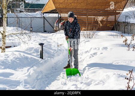 La cour était couverte de neige après une forte chute de neige. Un homme nettoie les chemins du jardin de la neige par une journée ensoleillée en hiver. Le jardinier s'occupe de la question Banque D'Images