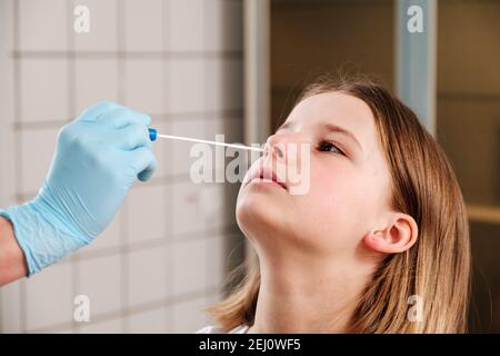 La main du médecin avec un coton-tige prend une analyse du nez d'une fille. Banque D'Images