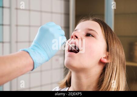 La main du médecin avec un coton-tige prend une analyse de la bouche d'une fille. Banque D'Images