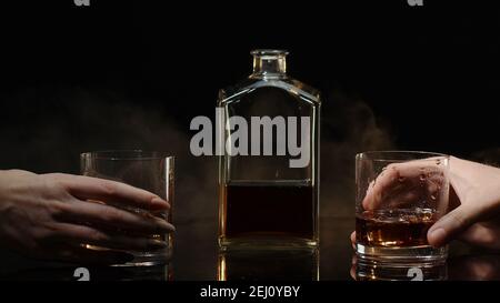 Deux mains avec des verres de whisky cognac et des glaçons pour des encouragements sur fond noir. Célébration de la réussite d'affaires, Noël, anniversaire, anniversaire. Porter des toasts avec des verres de brandy et de rhum Banque D'Images
