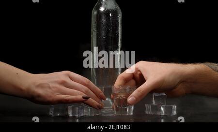 Barman déversant deux doses de vodka avec des glaçons dans une bouteille dans des verres sur fond noir. Deux mains avec des verres de vodka faisant Santé. Porter des toasts avec des verres de tequila ou du saké Banque D'Images