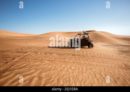 Une femme pilote en casque, à bord d'un quad noir, avec drapeaux emirates sur les dunes de sable safari, pour s'amuser en plein air Banque D'Images