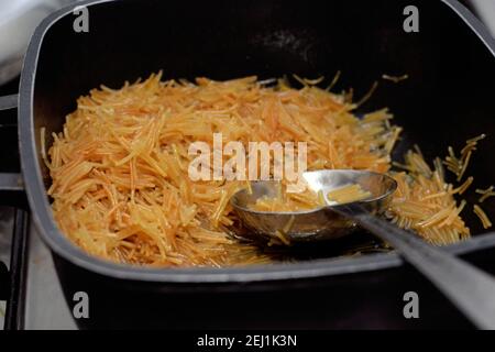 Bruni dans du beurre doux vermicelles égyptiennes cuites avec de l'eau et du sucre dans une casserole avec une louche,. Dessert égyptien traditionnel Banque D'Images