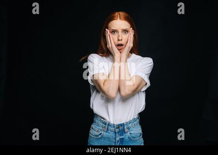 Une jeune femme effrayée et choquée porte un T-shirt et un pantalon en denim debout avec bouche ouverte Banque D'Images