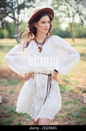 Mode extérieur: La belle jeune fille boho (hippie) dans grove (forêt). Portrait d'une femme adorable en robe blanche et chapeau Banque D'Images