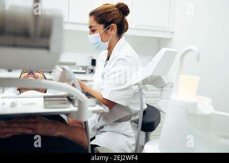 Dentiste de sexe féminin examinant les dents de la patiente. Médecin dentaire utilisant des outils pour vérifier les dents d'un homme assis dans la chaise du dentiste/ Banque D'Images