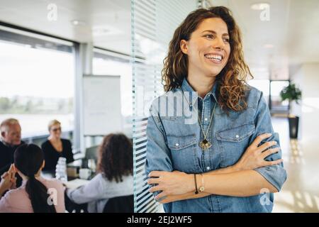 Portrait d'une femme d'affaires heureuse qui regarde loin et souriait avec ses collègues dans la salle de réunion. Femme souriante avec collègues dans la salle de conférence ayant une réunion. Banque D'Images