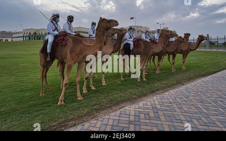 Hommes arabes en costume traditionnel à cheval et debout dans les chameaux Avant de l'Amiri diwan à Doha Qatar après-midi tourné avec des nuages dans le ciel Banque D'Images