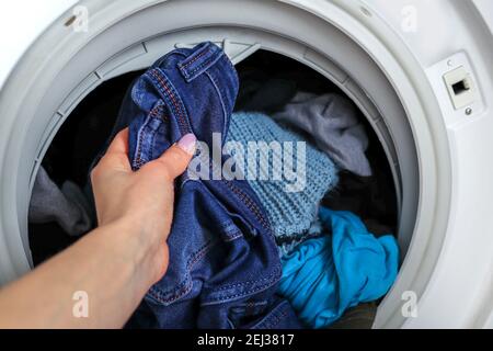 Main féminine sortant des vêtements propres jeans d'un lavage machine à la maison Banque D'Images