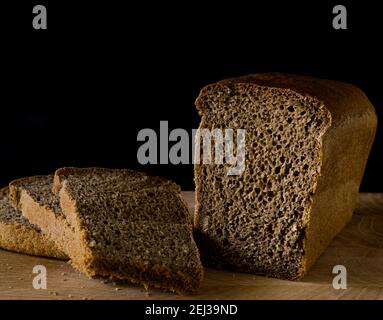 Pain de seigle noir, coupé en morceaux, en forme de brique sur une planche de bois, sur fond noir Banque D'Images