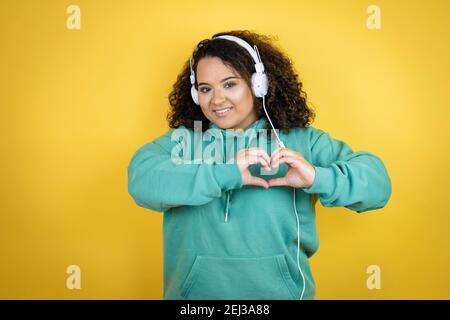 Jeune fille afro-américaine portant des vêtements de sport et utilisant des écouteurs sourire en amour montrant le symbole du coeur et la forme avec les mains Banque D'Images