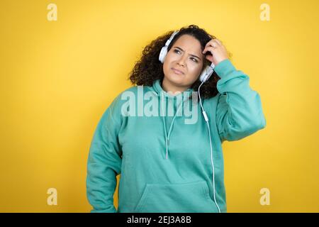 Une jeune fille afro-américaine portant des vêtements de gym et utilisant des écouteurs confond et se demande des questions. Incertain avec le doute, pensant avec la main sur lui Banque D'Images