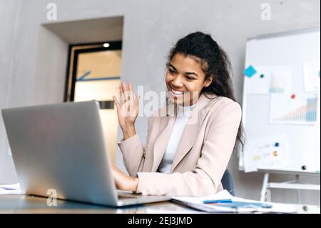 Une jeune femme d'affaires très occupée communique par vidéoconférence. Une employée noire multiethnique est assise au bureau, à l'aide d'un ordinateur portable, agite la main, parle par appel vidéo Banque D'Images