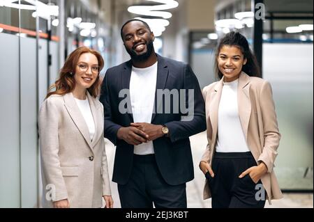 Des collègues qui réussissent en toute confiance se trouvent dans un bureau moderne. Portrait de gens d'affaires souriants multiethniques en tenue formelle. Les employés amicaux, hommes et femmes, regardent le concept de caméra et de travail d'équipe Banque D'Images