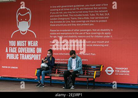 PUTNEY LONDON, ROYAUME-UNI, 21 FÉVRIER 2021. Passagers assis devant une grande affiche à la station de métro Putney. Tous les passagers voyageant en transports en commun sont maintenant tenus de porter des revêtements de visage dans le cadre des directives gouvernementales qui sont devenues obligatoires en juin 2020. Credit amer ghazzal/Alamy Live News Banque D'Images