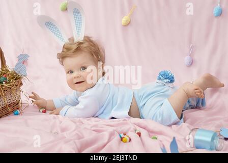 Joli petit bébé en costume de lapin sur couverture rose sur nous et souriant Banque D'Images