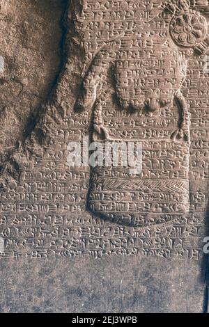 Ancienne cuneiforme assyrienne sculptée sur un mur de pierre sur la main humaine grugeage Banque D'Images