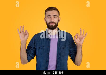 Concept de soulagement de contrainte. Beau jeune homme méditant avec les yeux fermés, gardant le calme sur fond orange studio Banque D'Images