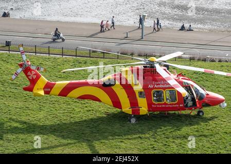 Southend on Sea, Essex, Royaume-Uni. 21 février 2021. L'ambulance aérienne Essex & Herts AgustaWestland AW169 enregistrement de l'hélicoptère G-HHEM débarqua sur les Cliff Gardens au-dessus de l'Esplanade occidentale sur le front de mer de Southend. Il a attiré des gens qui étaient dehors appréciant le temps chaud et ensoleillé de façon insaisonnière Banque D'Images