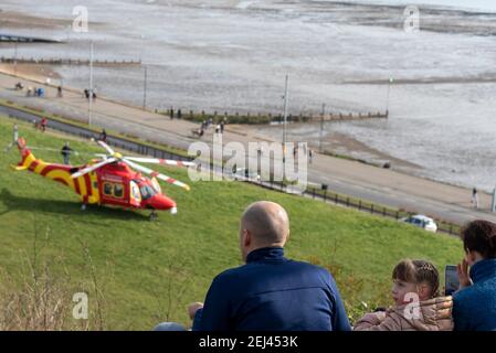 Southend on Sea, Essex, Royaume-Uni. 21 février 2021. L'ambulance aérienne Essex & Herts AgustaWestland AW169 enregistrement de l'hélicoptère G-HHEM débarqua sur les Cliff Gardens au-dessus de l'Esplanade occidentale sur le front de mer de Southend. Il a attiré des gens qui étaient dehors appréciant le temps chaud et ensoleillé de façon insaisonnière Banque D'Images