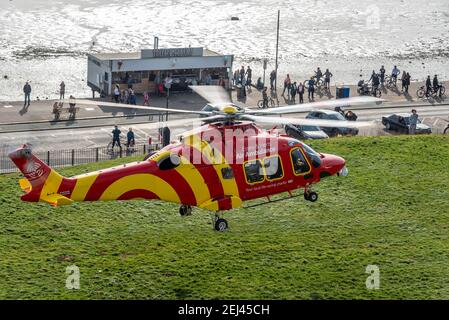 Southend on Sea, Essex, Royaume-Uni. 21 février 2021. L'ambulance aérienne Essex & Herts AgustaWestland AW169 enregistrement de l'hélicoptère G-HHEM débarqua sur les Cliff Gardens au-dessus de l'Esplanade occidentale sur le front de mer de Southend. Il a attiré des gens qui étaient dehors appréciant le temps chaud et ensoleillé de façon insaisonnière Banque D'Images