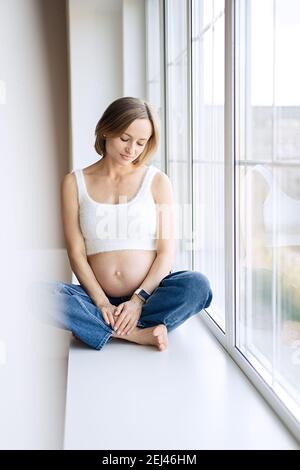 Femme enceinte assise près de la fenêtre à la maison Banque D'Images