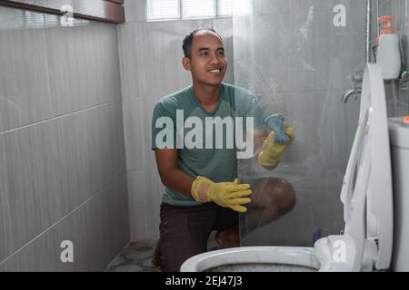 un homme portant des gants a nettoyé le séparateur en verre des toilettes la salle de bains Banque D'Images